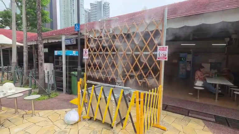 Fine mist spraying from trellis-mounted nozzles beside an open-air food centre, shown in a still from the demonstration video.